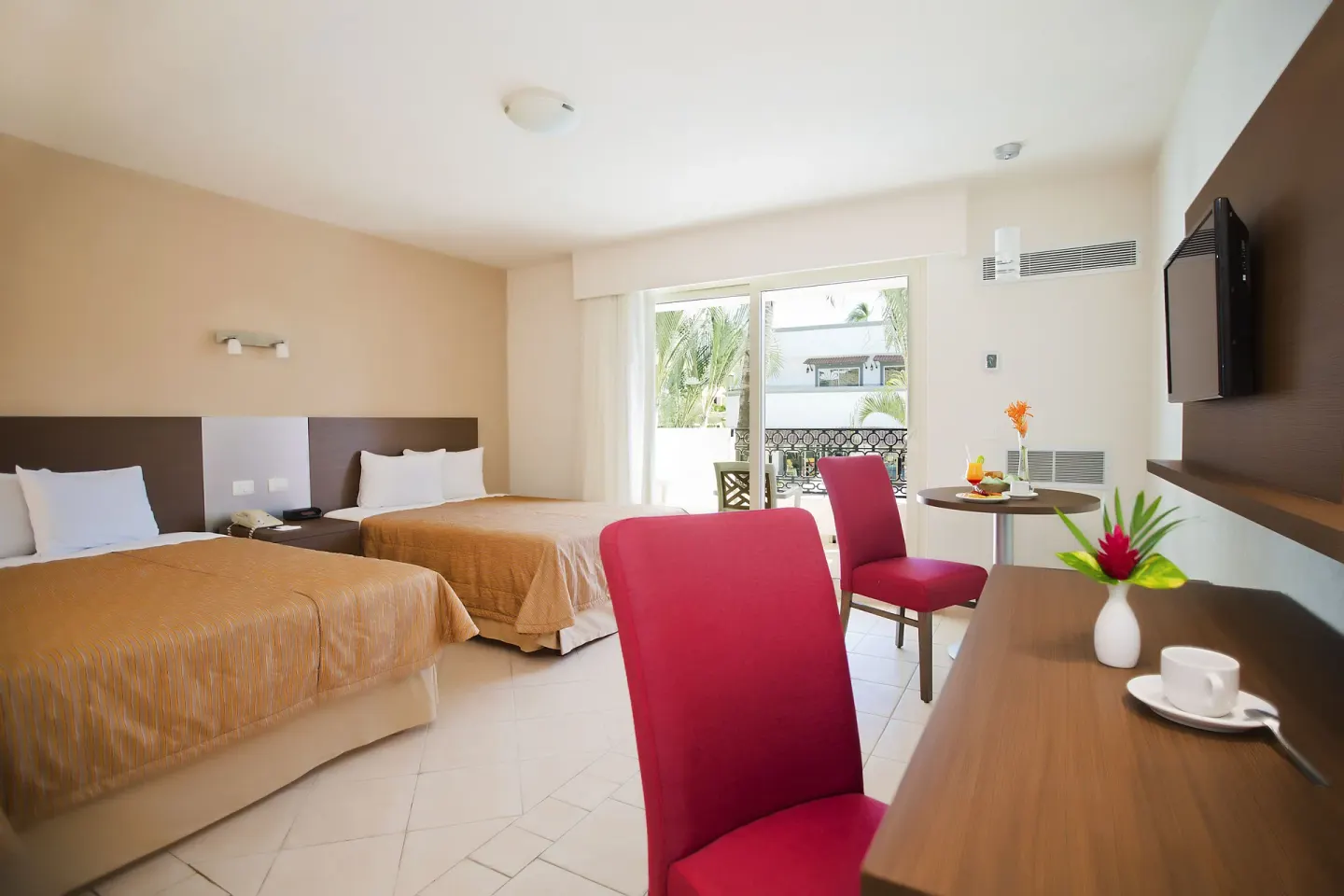 Guest room with two beds, red chairs, balcony doors and TV at Crown Paradise Club Puerto Vallarta.