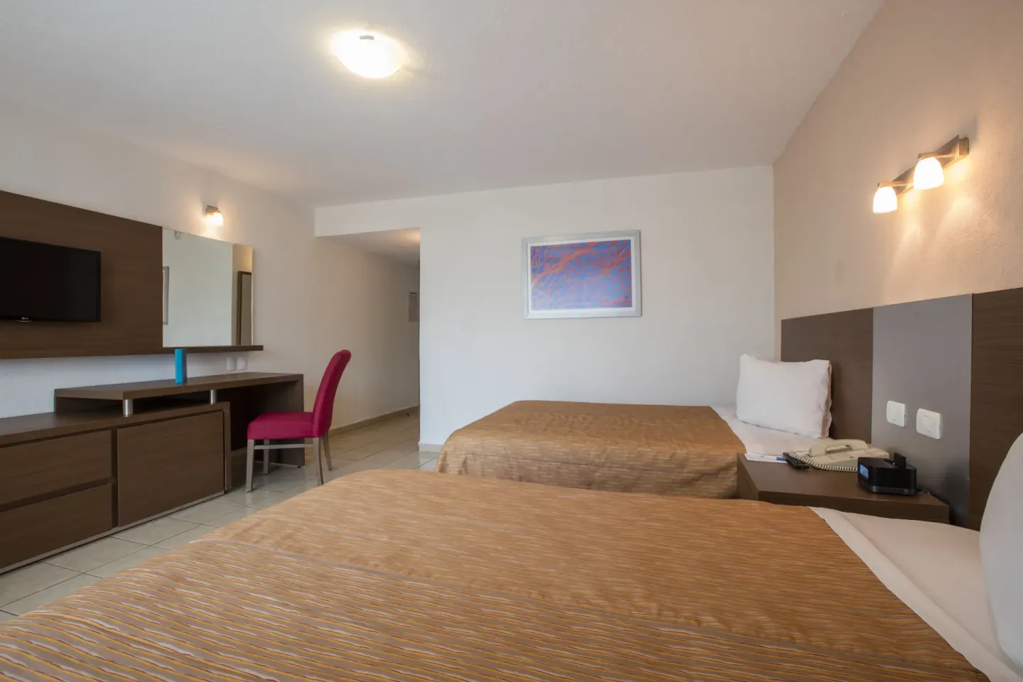 Guest room with two beds, desk, TV and pink chair at Crown Paradise Club Puerto Vallarta.