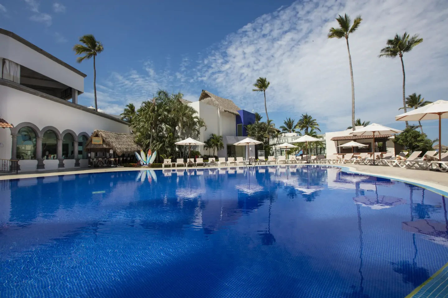 Large outdoor pool with loungers and palms at Crown Paradise Club Puerto Vallarta.