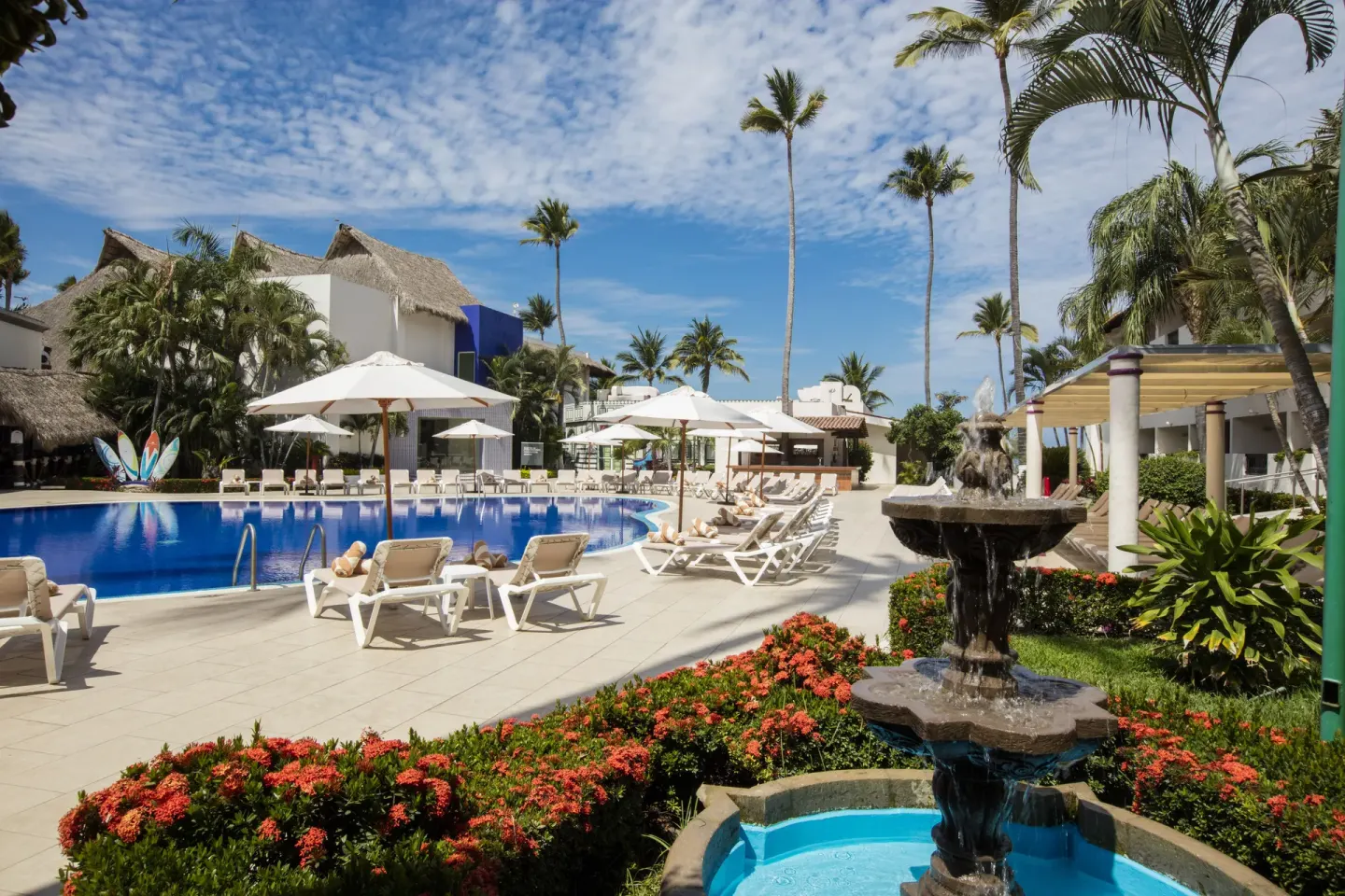 Pool deck with fountain, loungers, umbrellas, and palms at Crown Paradise Club Puerto Vallarta.