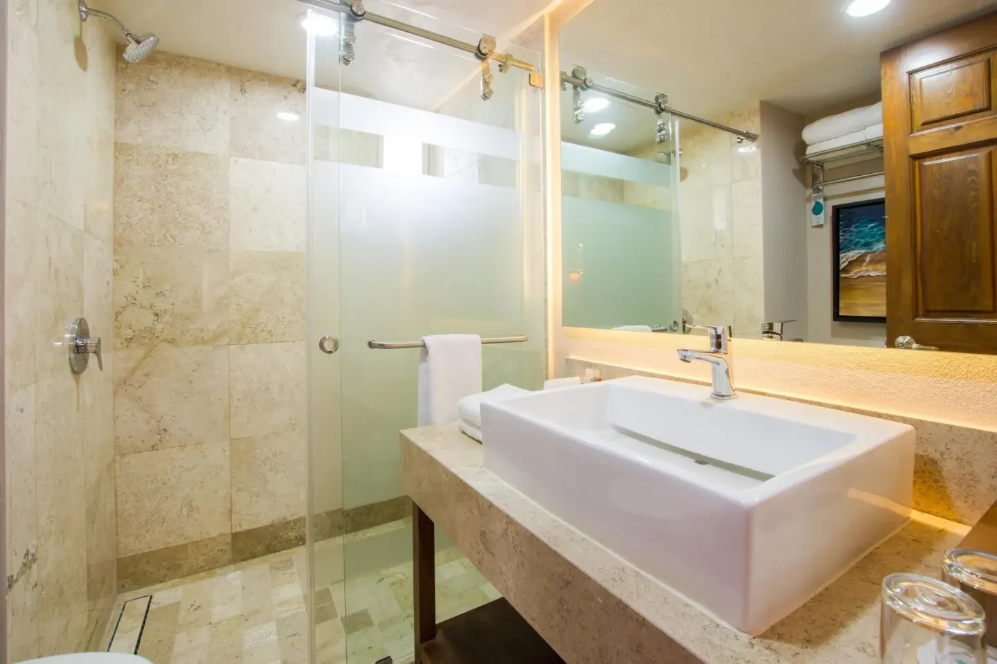 Stone-tile bathroom with glass shower and vessel sink at Crown Paradise Club Puerto Vallarta.