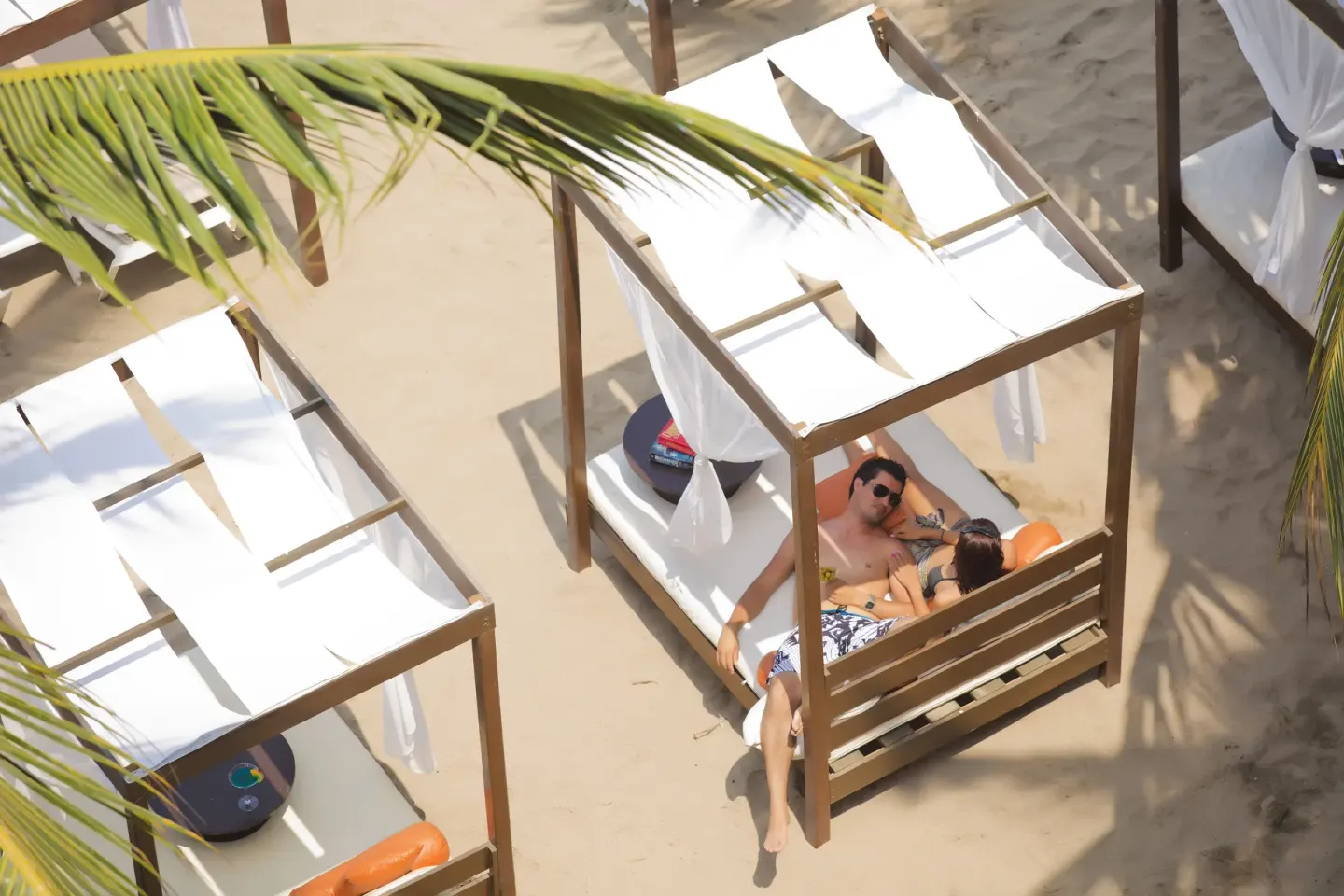 Beach cabanas with white cushions and palm fronds at Crown Paradise Golden Resort.