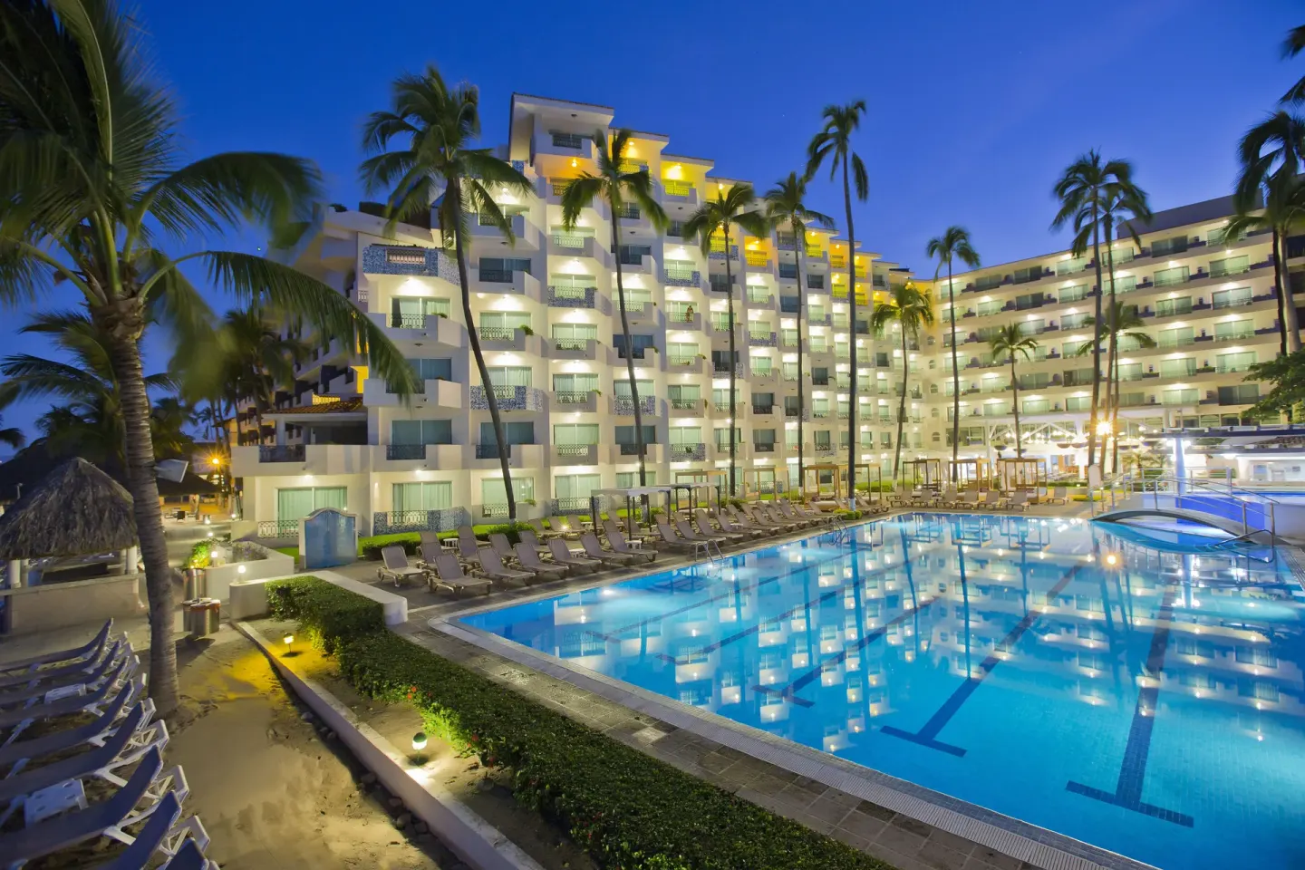 Evening pool with lit hotel balconies and palm trees at Crown Paradise Golden Resort.