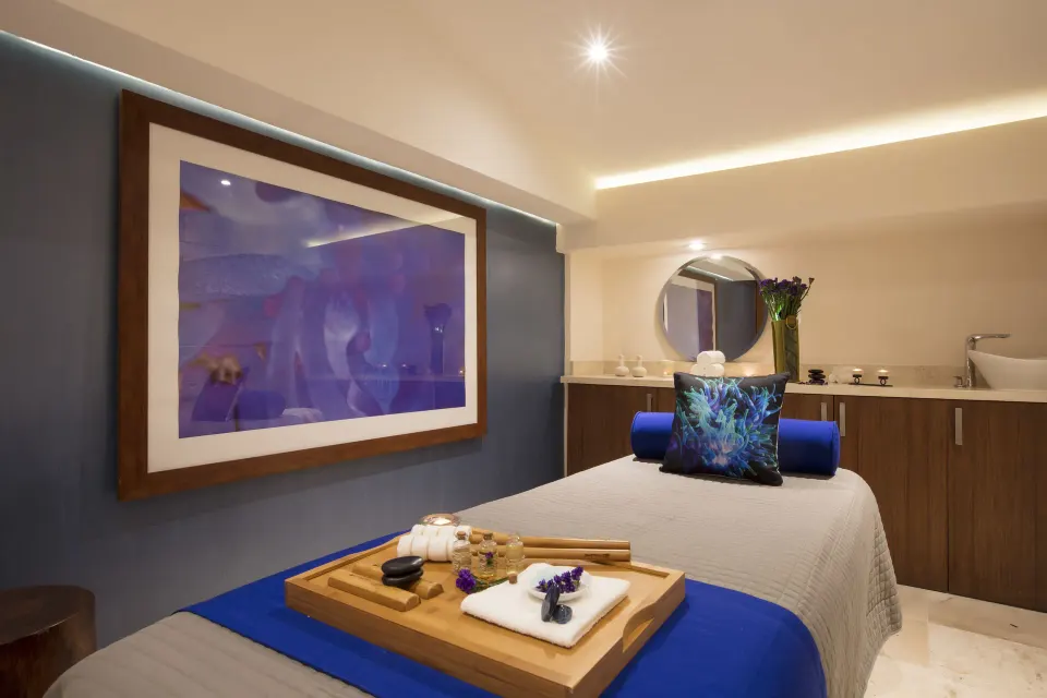 Spa treatment room with blue linens, wall art, candles, and vanity at Crown Paradise Golden Resort.