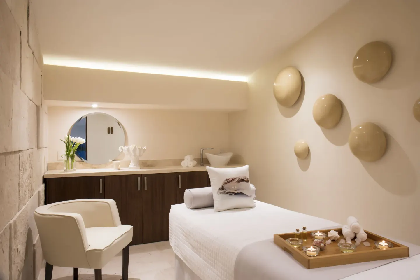 Spa treatment room with massage bed, candles, chair, and vanity at Crown Paradise Golden Resort.