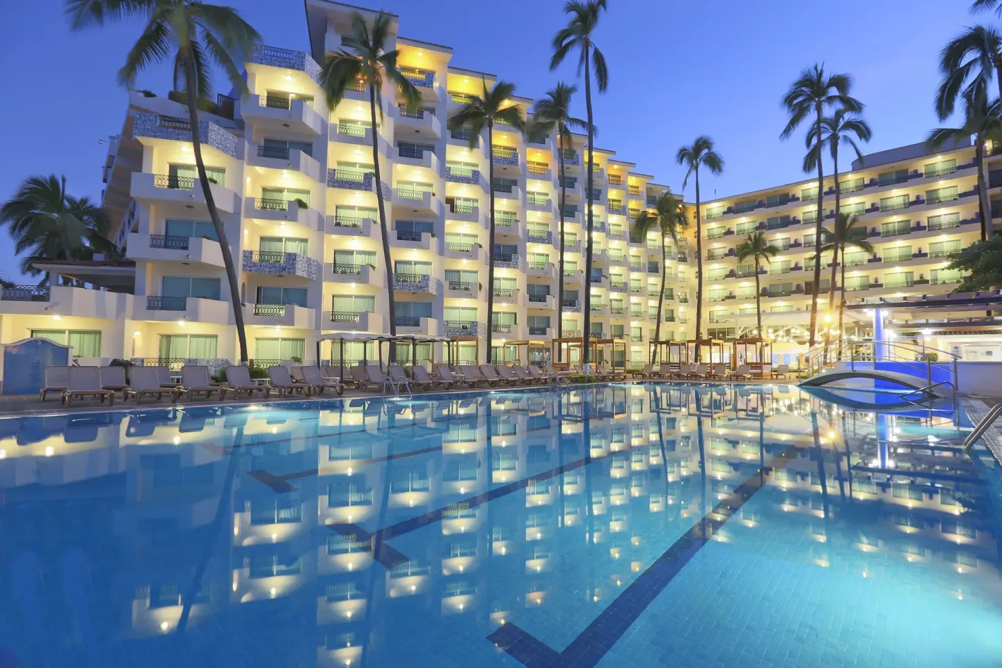 Twilight pool with bridge, lounge chairs, and lit balconies at Crown Paradise Golden Resort.