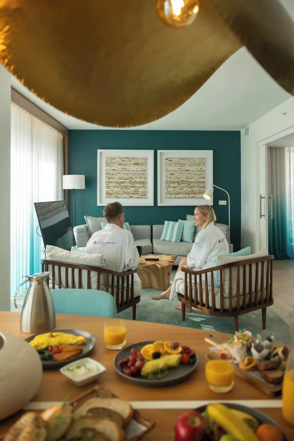 Couple in robes seated in a suite lounge with breakfast at Curacao Marriott Beach Resort.