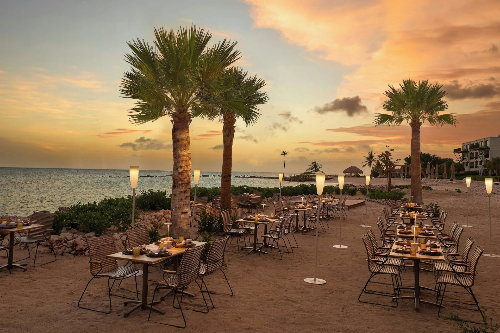 Beachfront dining tables at sunset beside the ocean at Curacao Marriott Beach Resort.