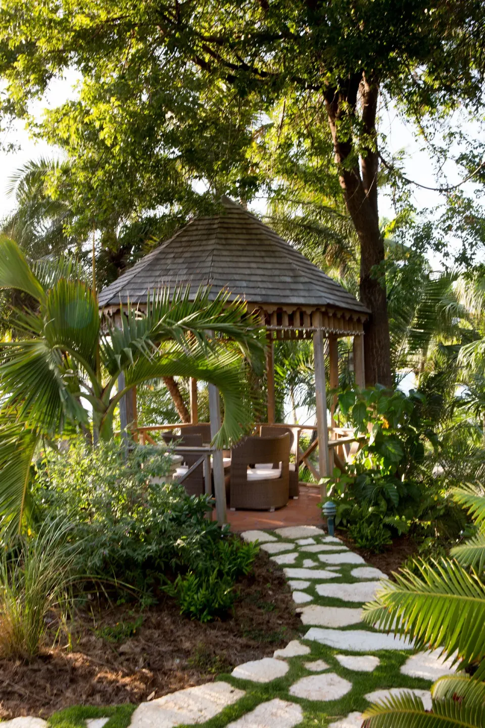 A garden gazebo sits along a stone path in lush greenery at Curtain Bluff Resort.