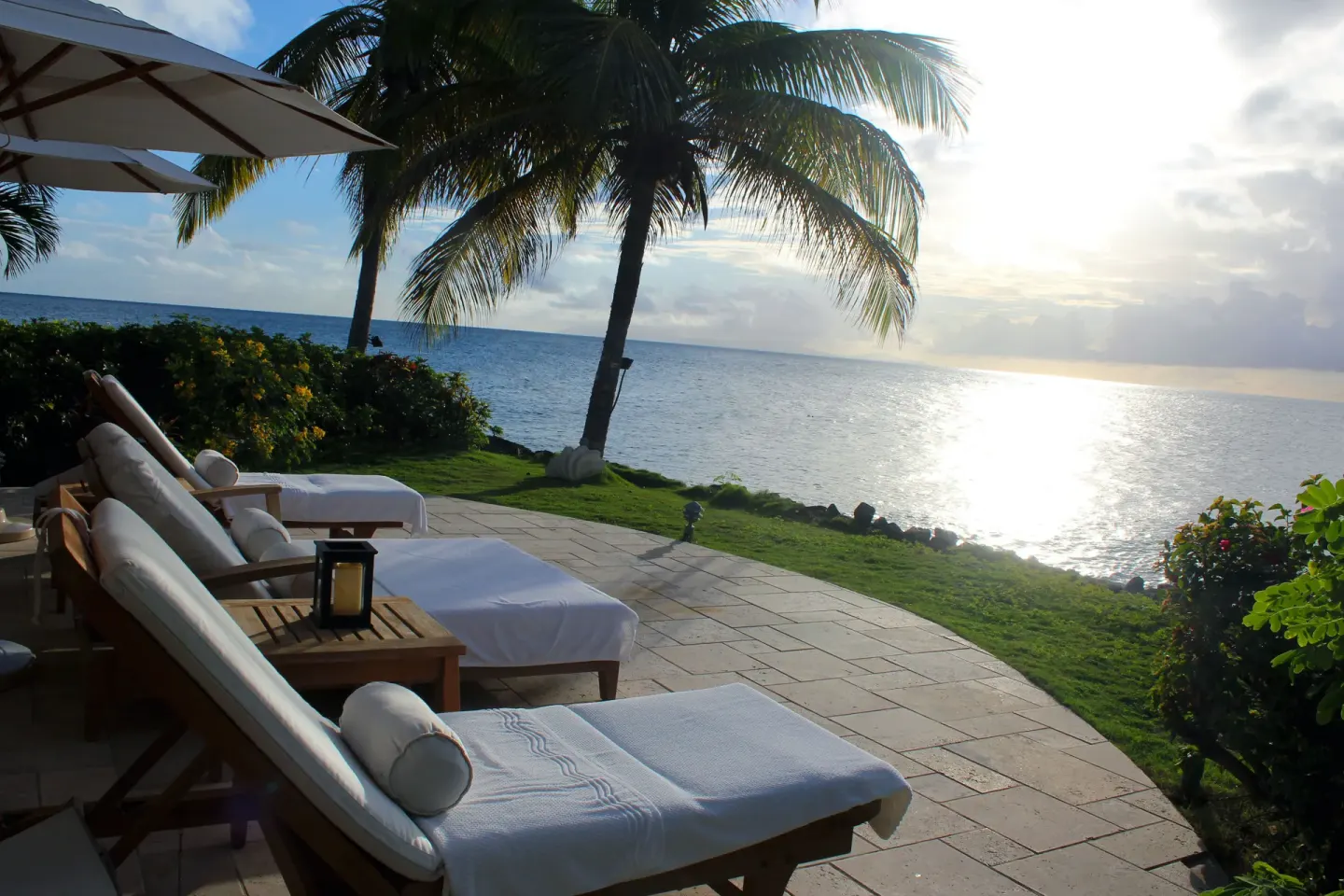 Oceanfront lounge chairs face the water and sunset beside palms at Curtain Bluff Resort.