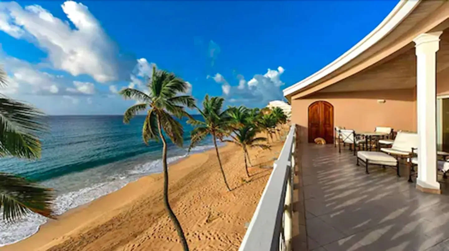A beachfront terrace overlooks palm trees and the ocean at Curtain Bluff Resort.