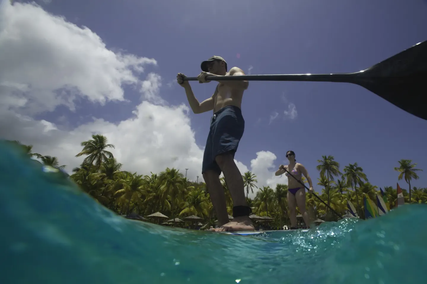 Guests paddleboard in clear water near a palm-lined beach at Curtain Bluff Resort.