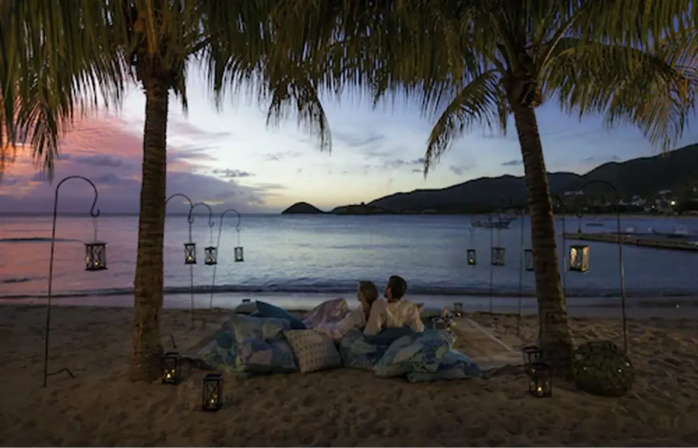 Guests sit on cushions under palm trees at sunset at Curtain Bluff Resort.