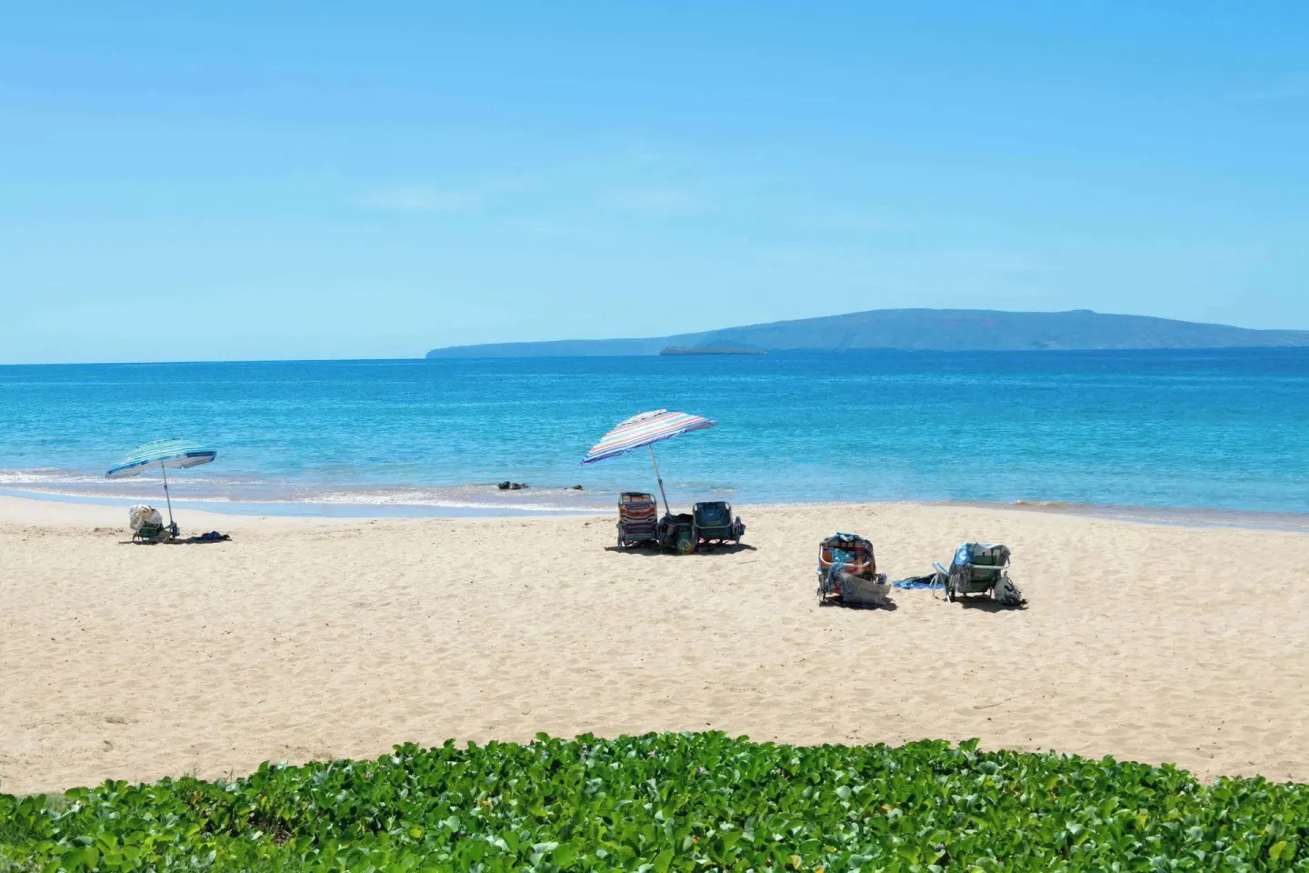 Beach chairs and umbrellas facing turquoise water near Days Inn Maui Oceanfront.