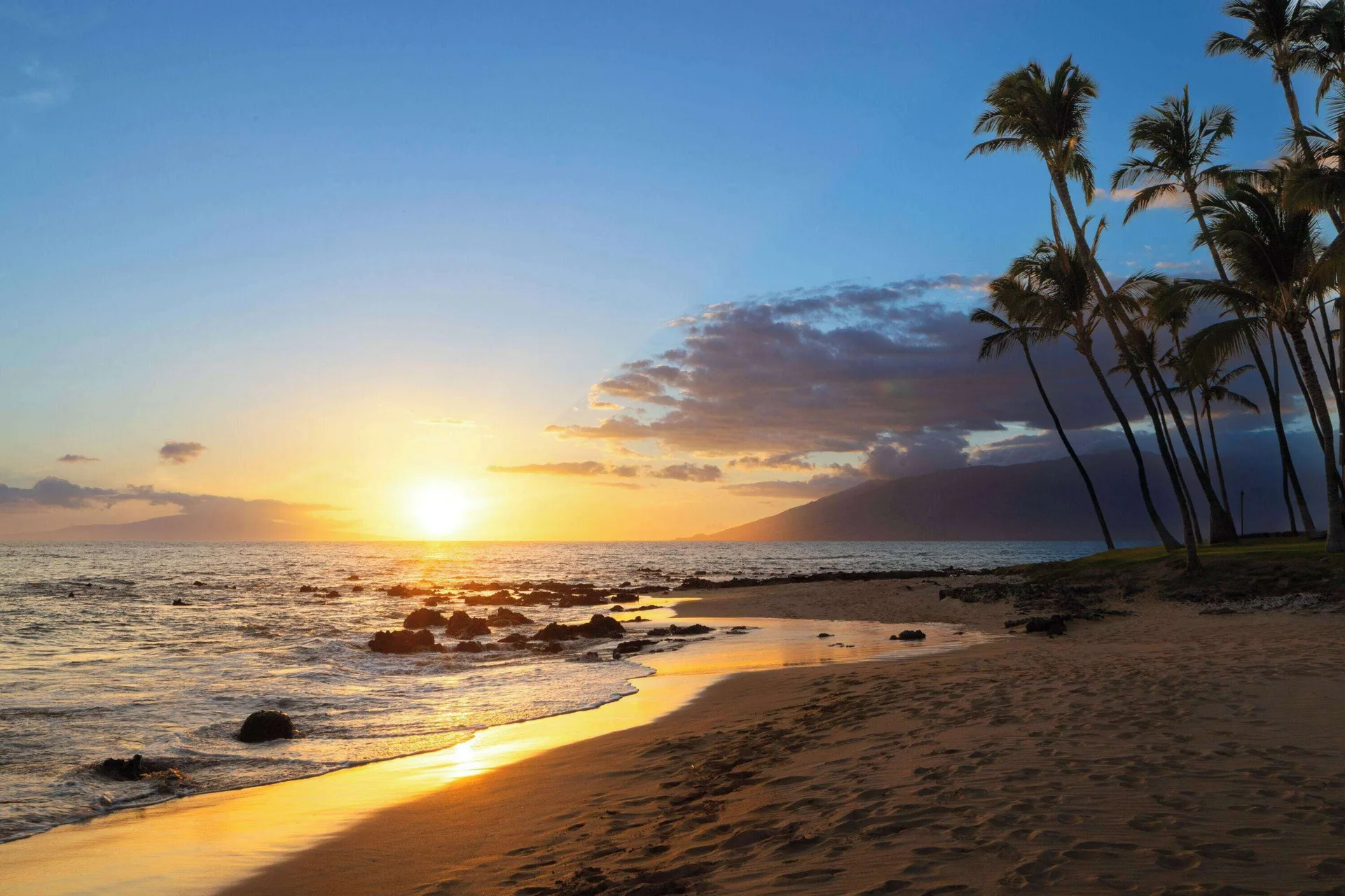 Sandy beach, ocean, rocks, and palm trees at sunset near Days Inn Maui Oceanfront.