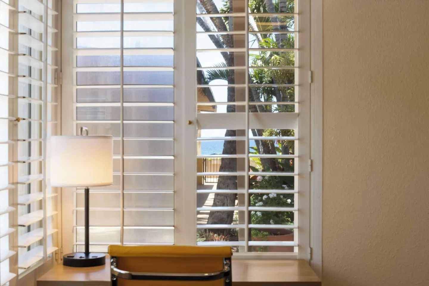 Desk, lamp, yellow chair, shutters, palms, and ocean beyond at Days Inn Maui Oceanfront.