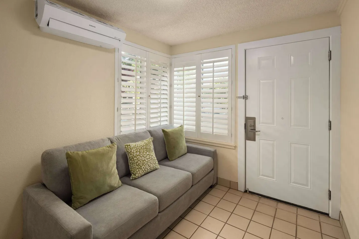 Entry sitting nook with gray sofa, green pillows, shutters, and door at Days Inn Maui Oceanfront.
