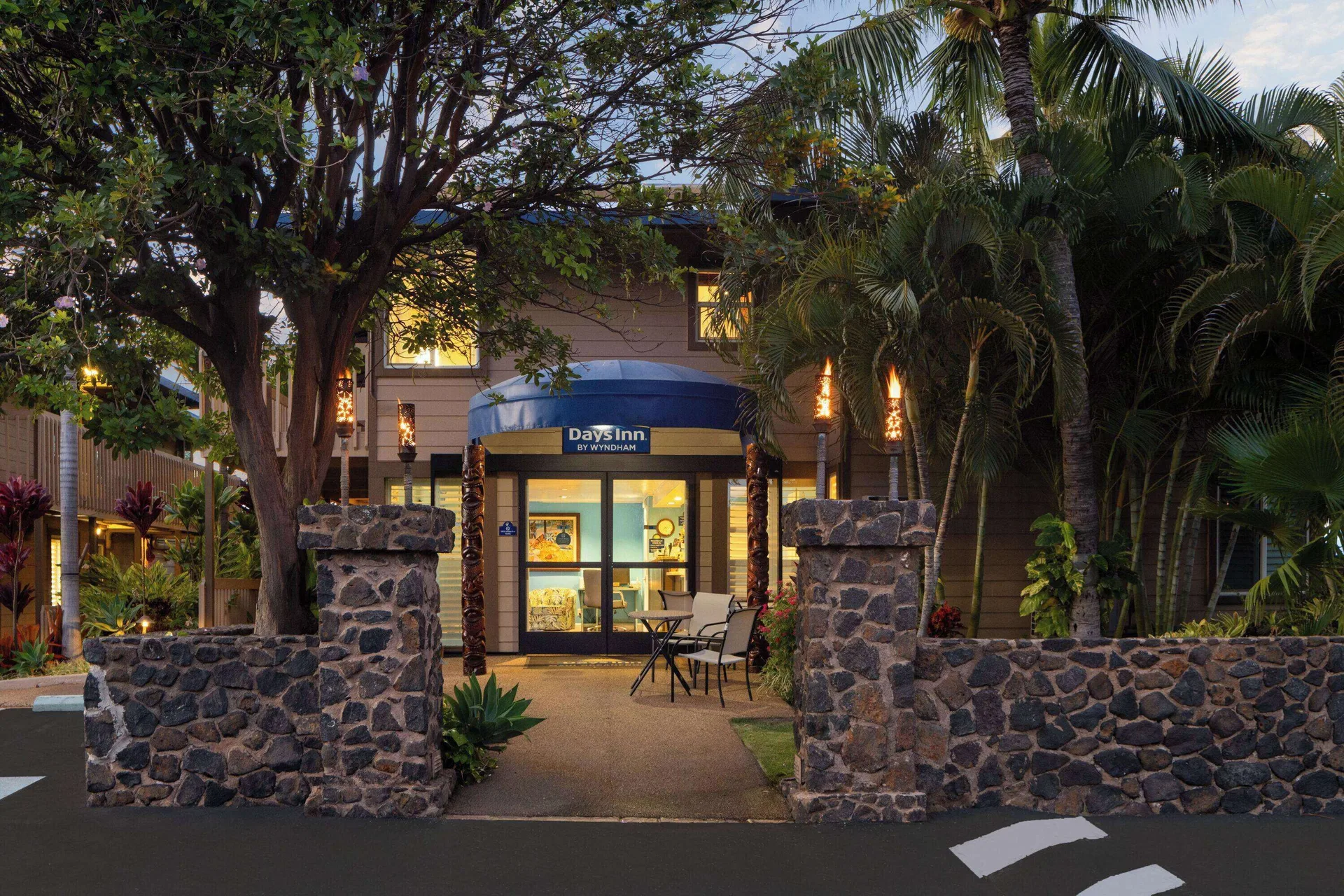 Illuminated entrance with stone walls and palms at Days Inn Maui Oceanfront.