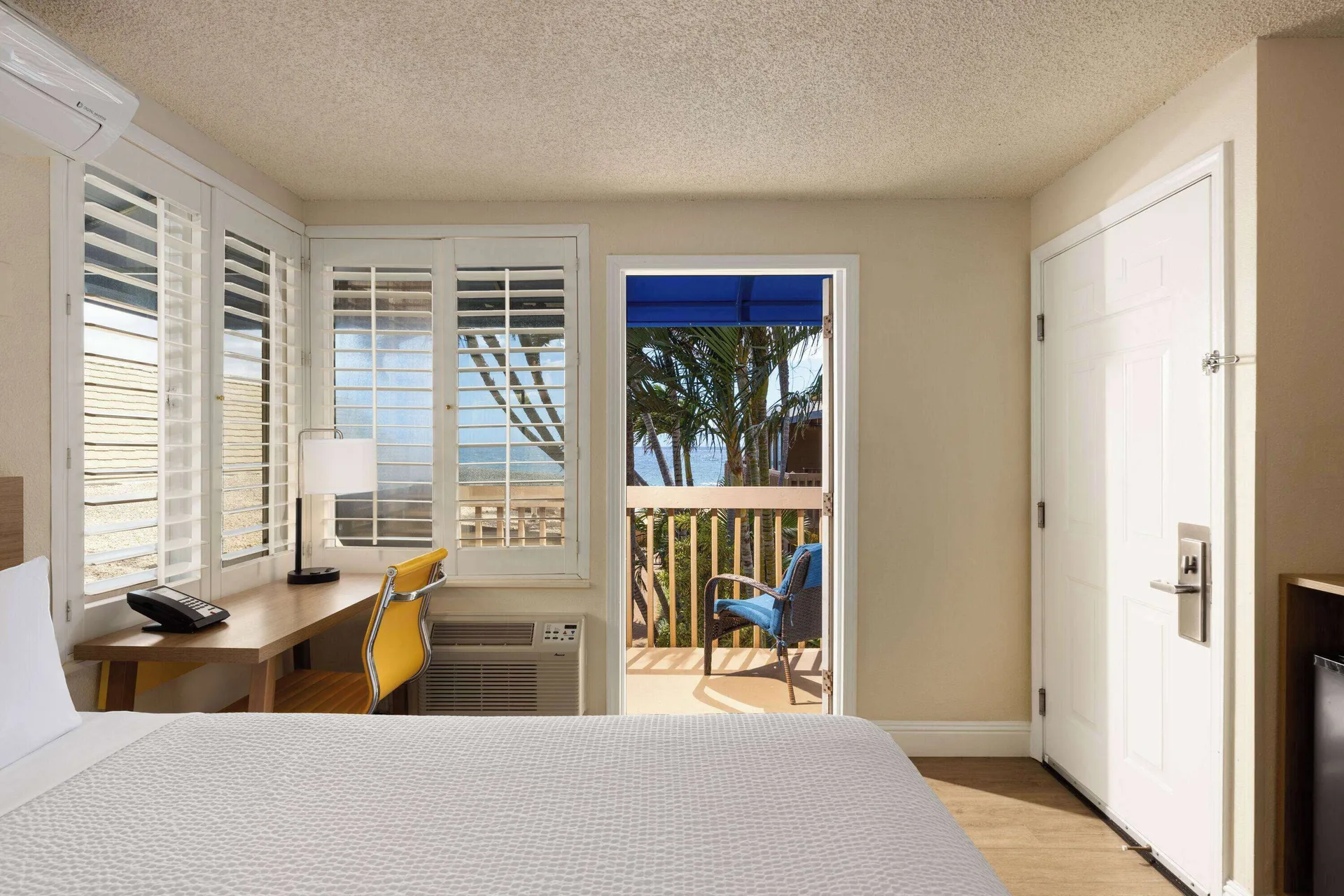 Guest room with white bed, desk, shutters, and balcony at Days Inn Maui Oceanfront.
