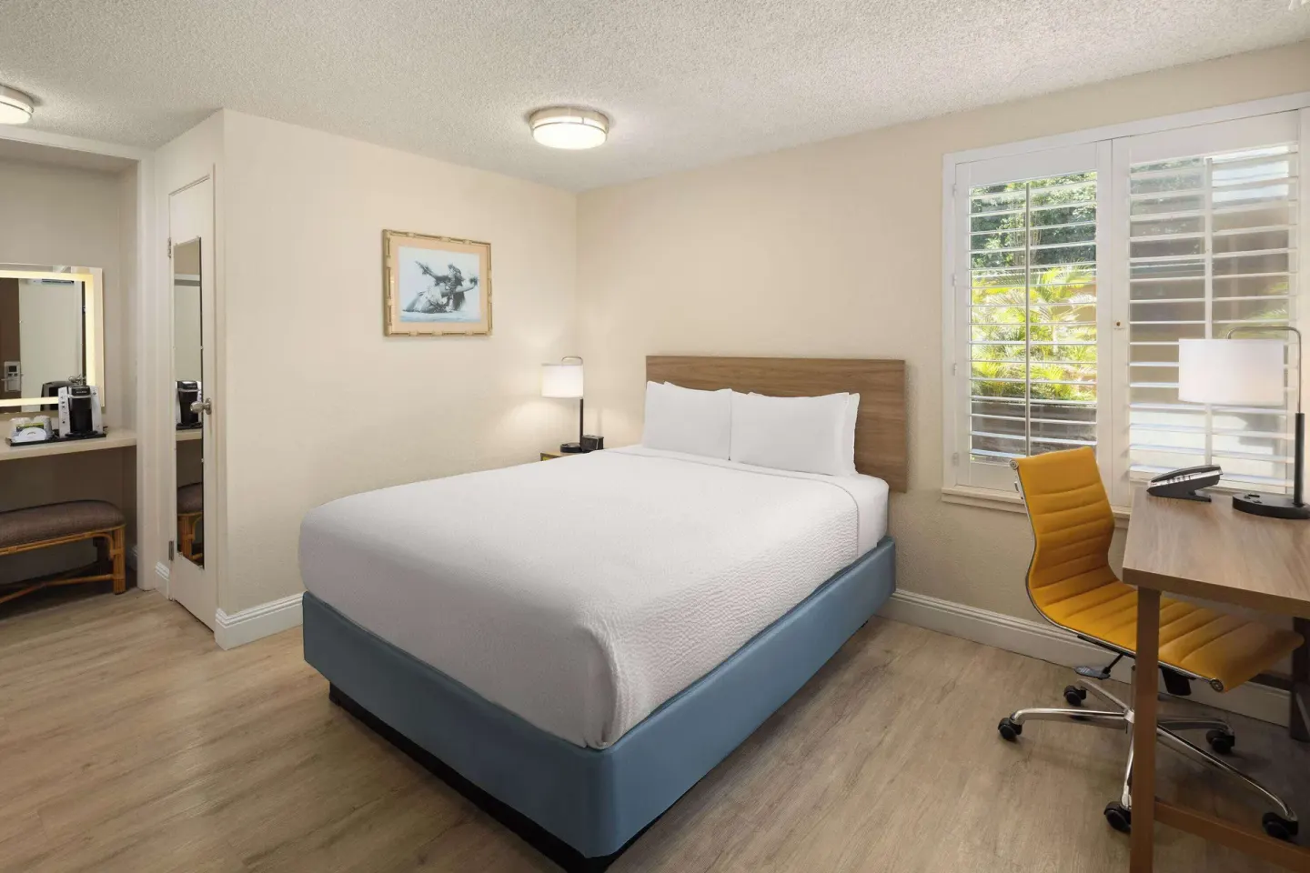 Guest room with one white bed, desk, shutters, and vanity area at Days Inn Maui Oceanfront.