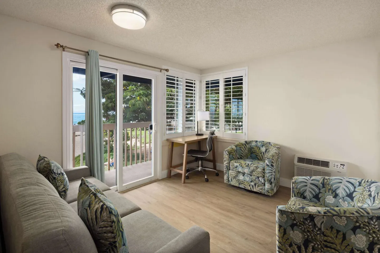 Living area with sofa, armchairs, desk, and balcony doors at Days Inn Maui Oceanfront.