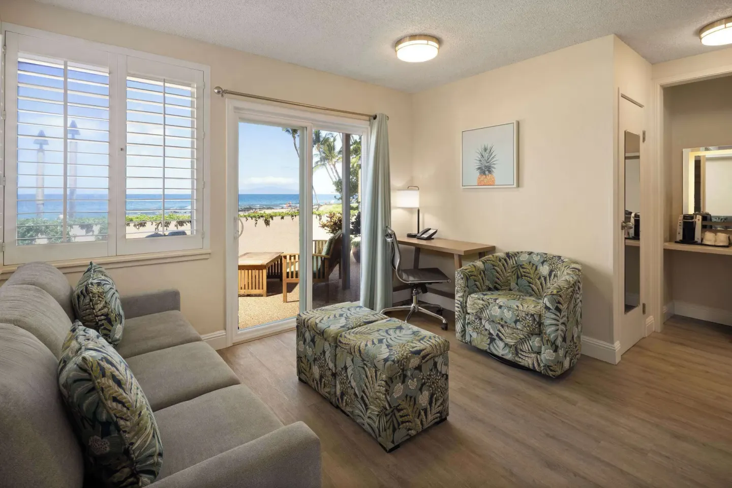 Living room with sofa, chair, desk, patio doors, and ocean view at Days Inn Maui Oceanfront.