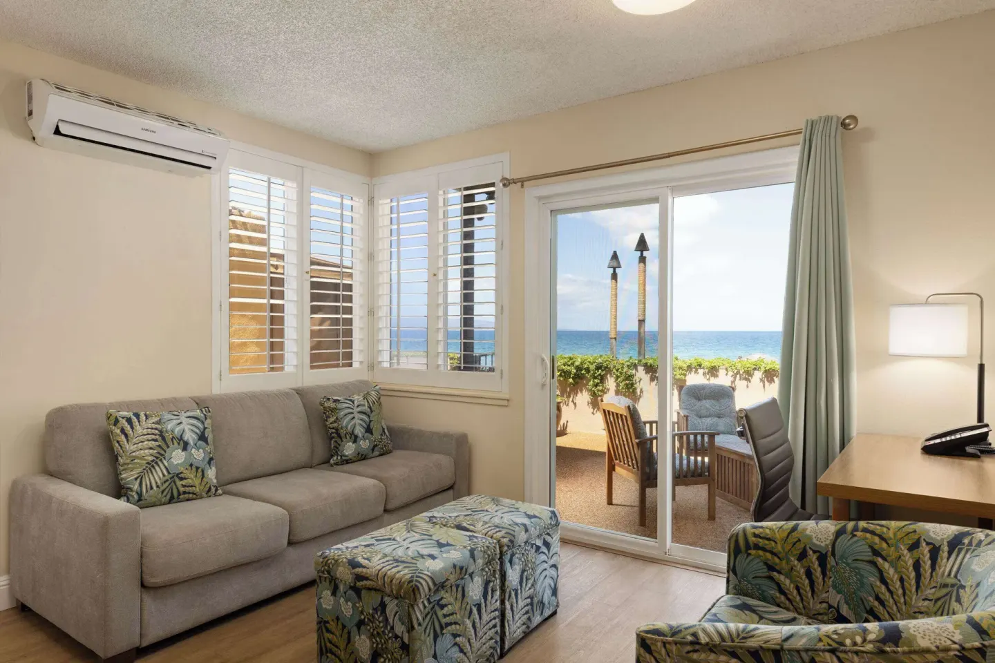 Living room with sofa, desk, patio seating, and ocean view at Days Inn Maui Oceanfront.