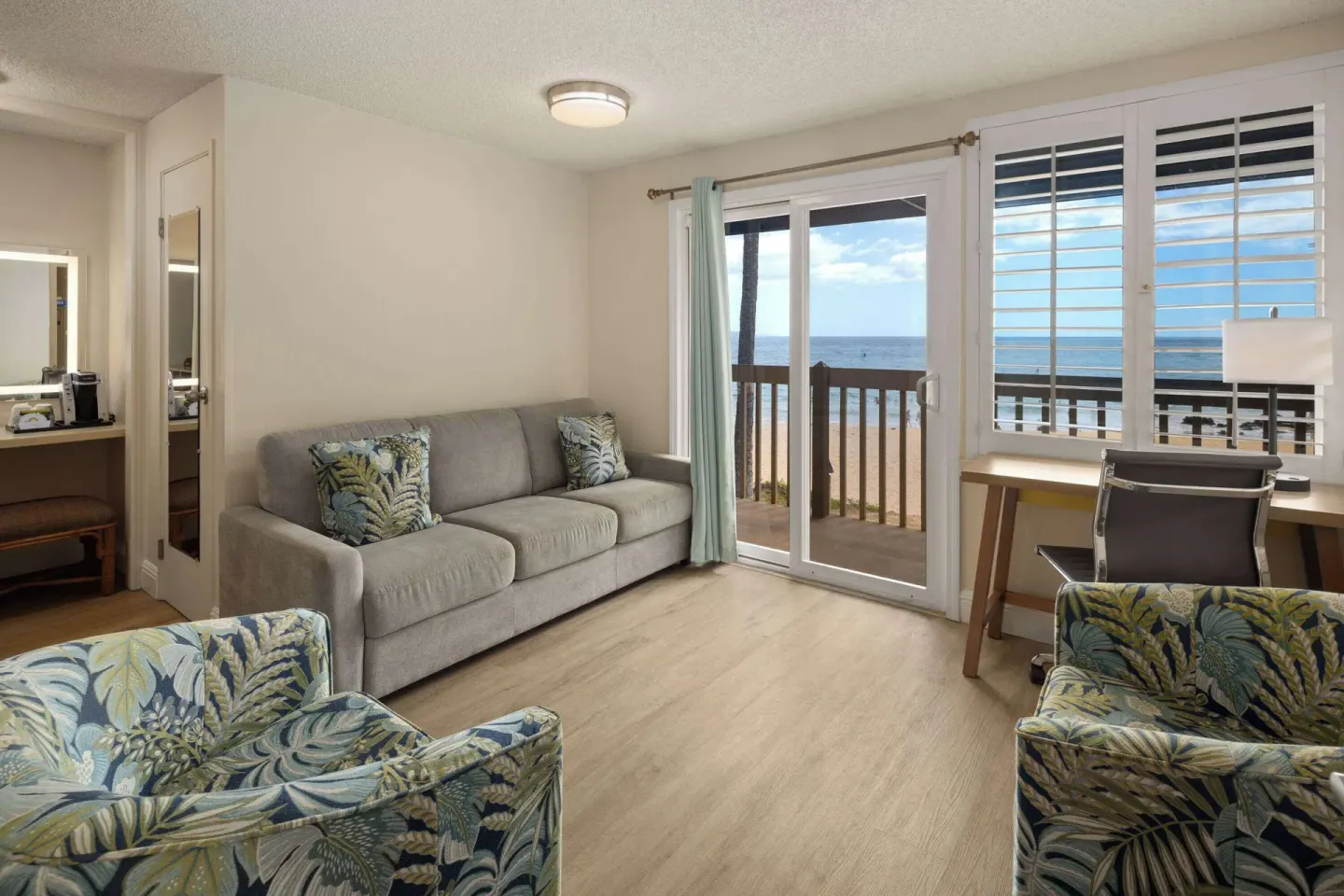Oceanfront sitting area with sofa, chairs, desk, and balcony at Days Inn Maui Oceanfront.