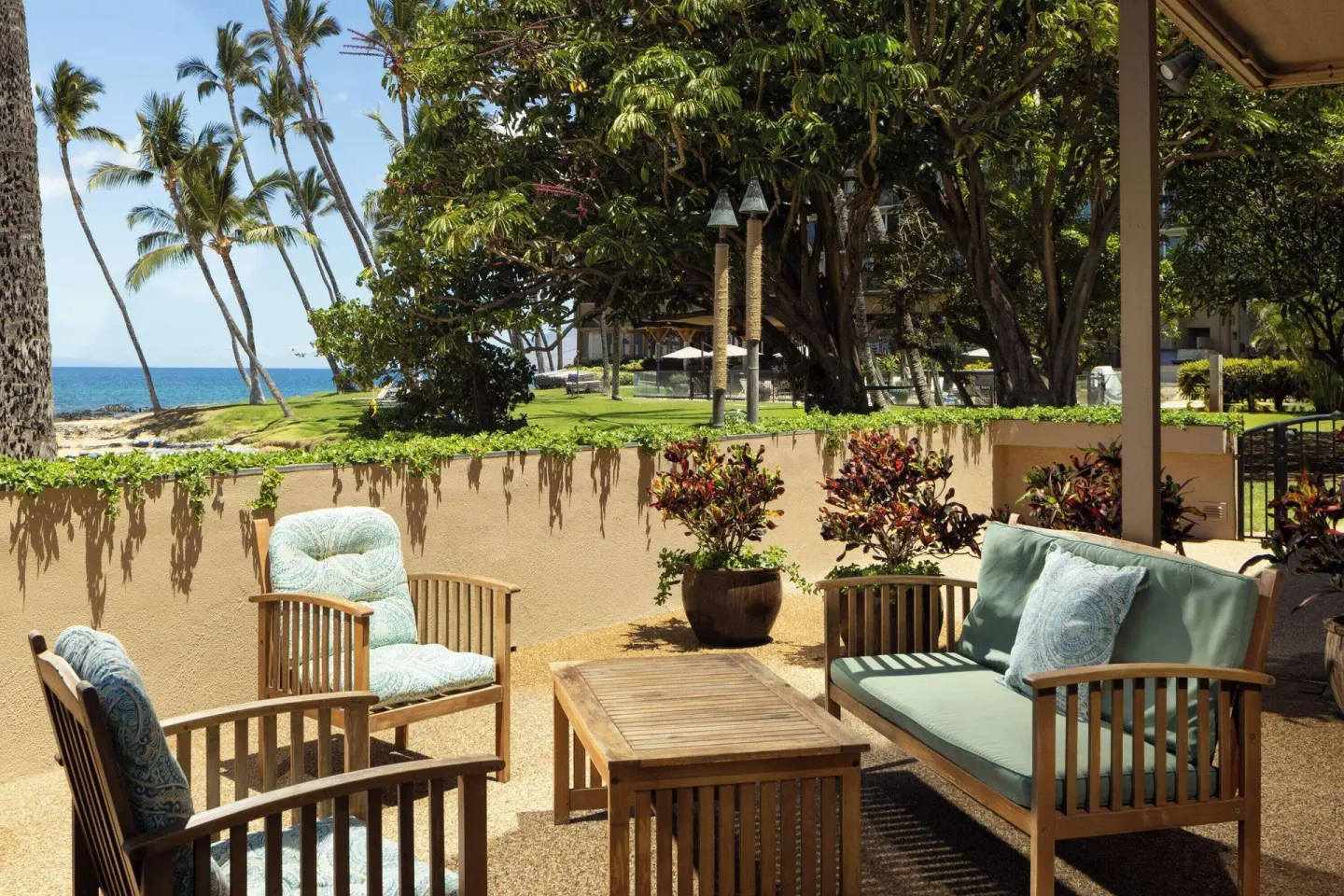 Outdoor patio seating with palm trees and ocean beyond at Days Inn Maui Oceanfront.