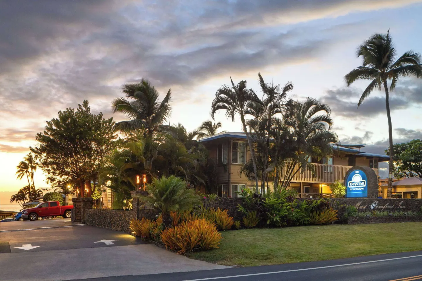 Days Inn Maui Oceanfront exterior, lawn, palms, and driveway at sunset.
