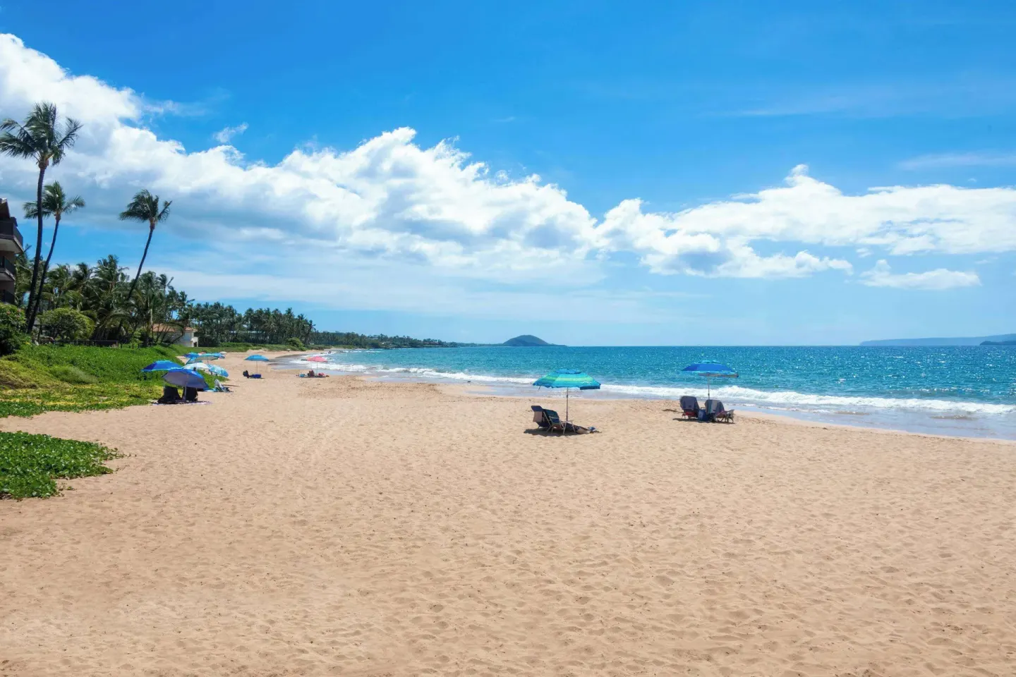 Wide sandy beach with ocean, umbrellas, and lounge chairs near Days Inn Maui Oceanfront.