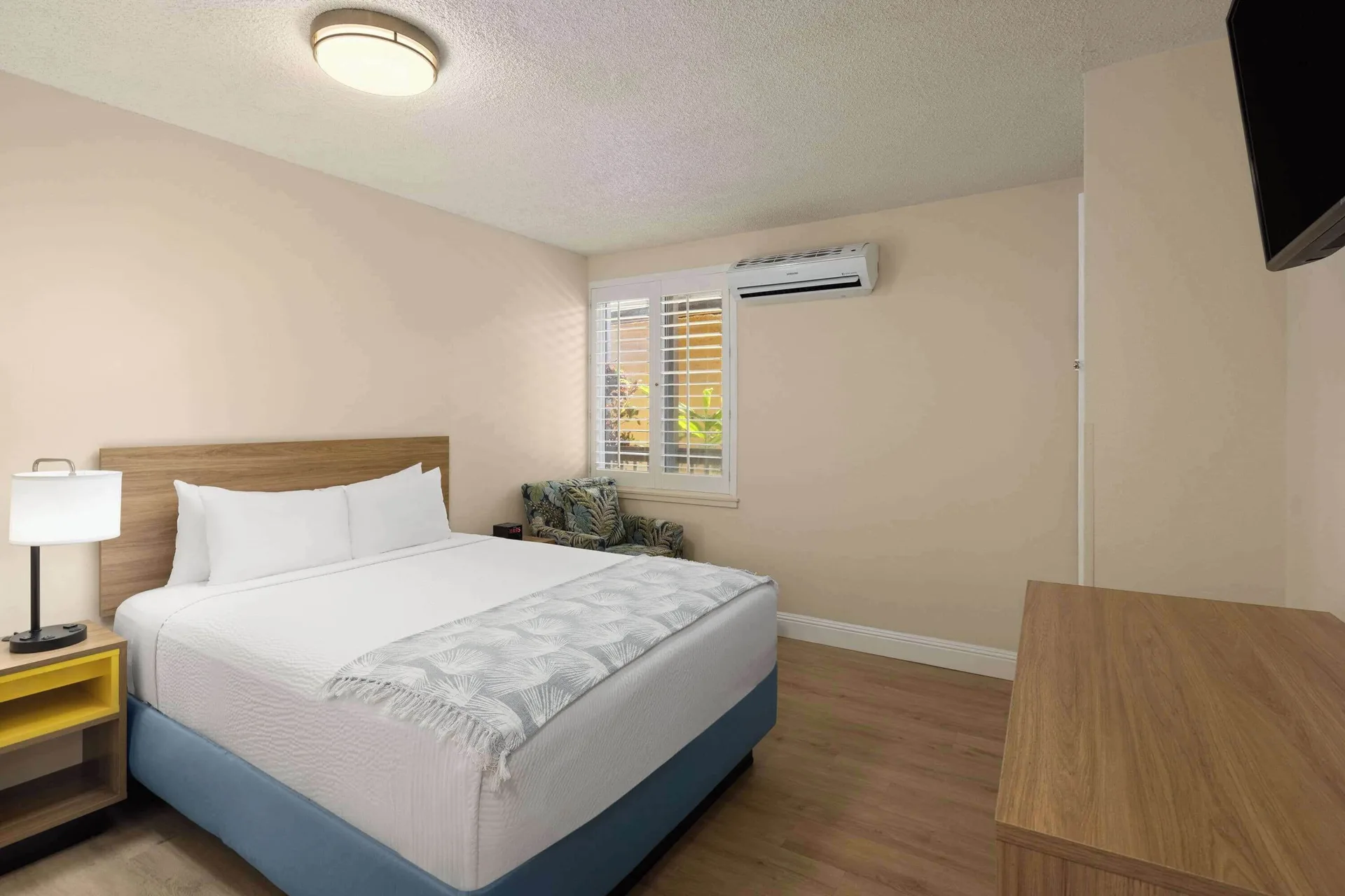 Bed, nightstand, window shutters, and wall TV in a suite bedroom at Days Inn Maui Oceanfront.