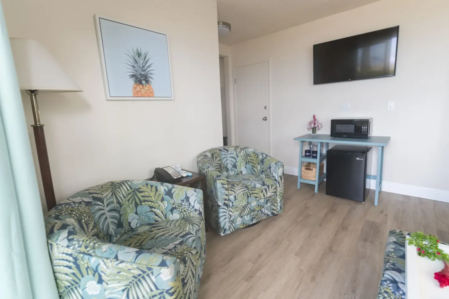 Two floral chairs, wall TV, mini fridge, and microwave in a suite at Days Inn Maui Oceanfront.