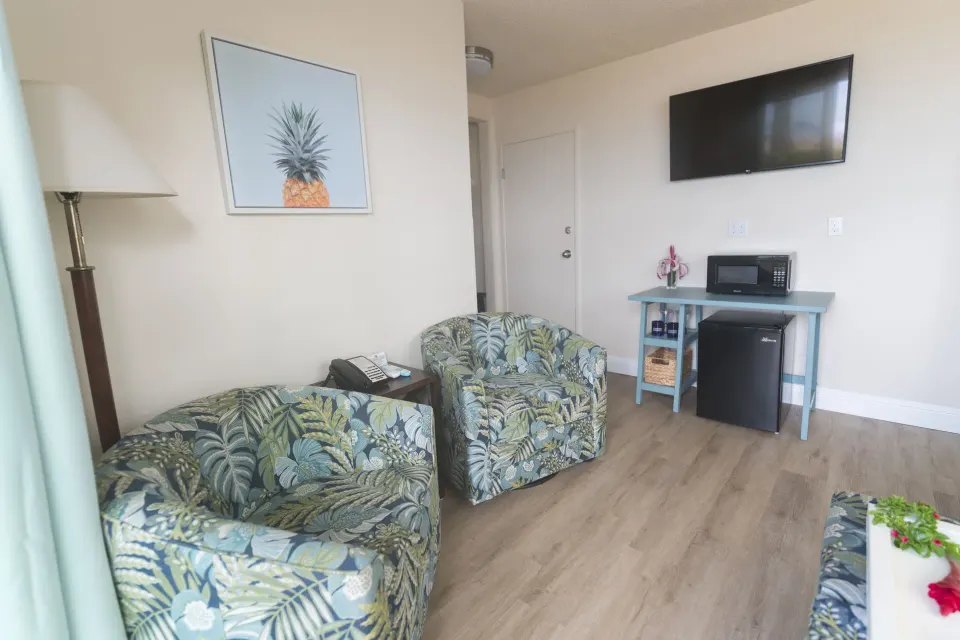 Two floral chairs, wall TV, mini fridge, and microwave in a suite at Days Inn Maui Oceanfront.