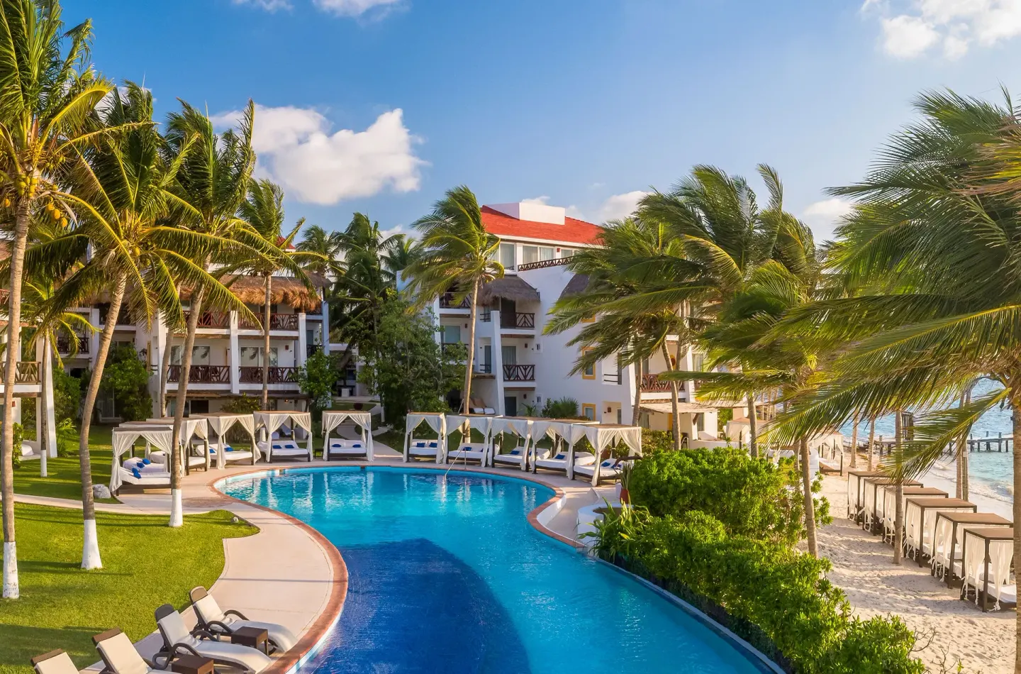 Curving pool beside the beach and palms at Desire Pearl Riviera Maya Resort.