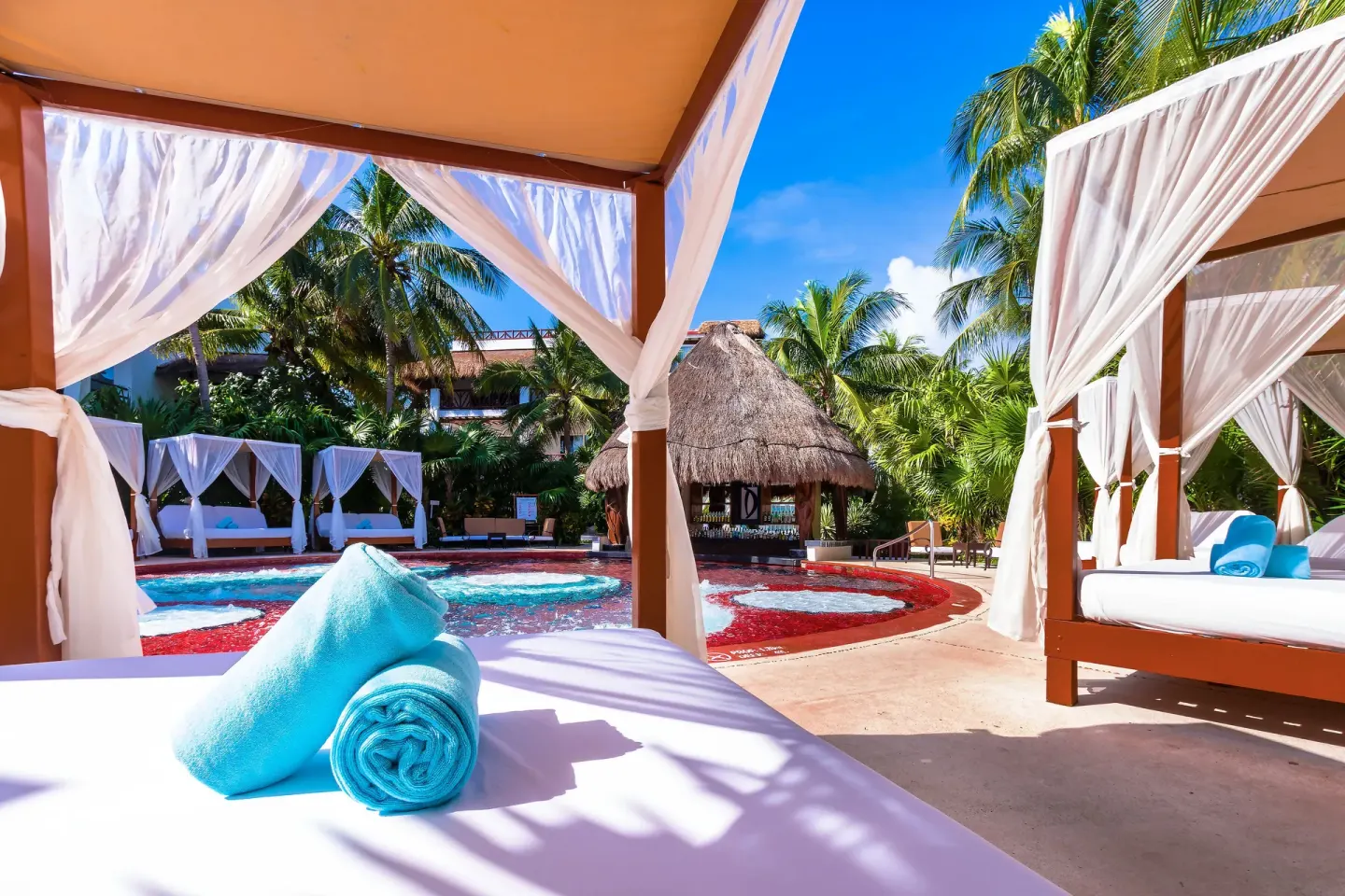 Canopied daybeds beside a red-edged spa pool at Desire Pearl Riviera Maya Resort.