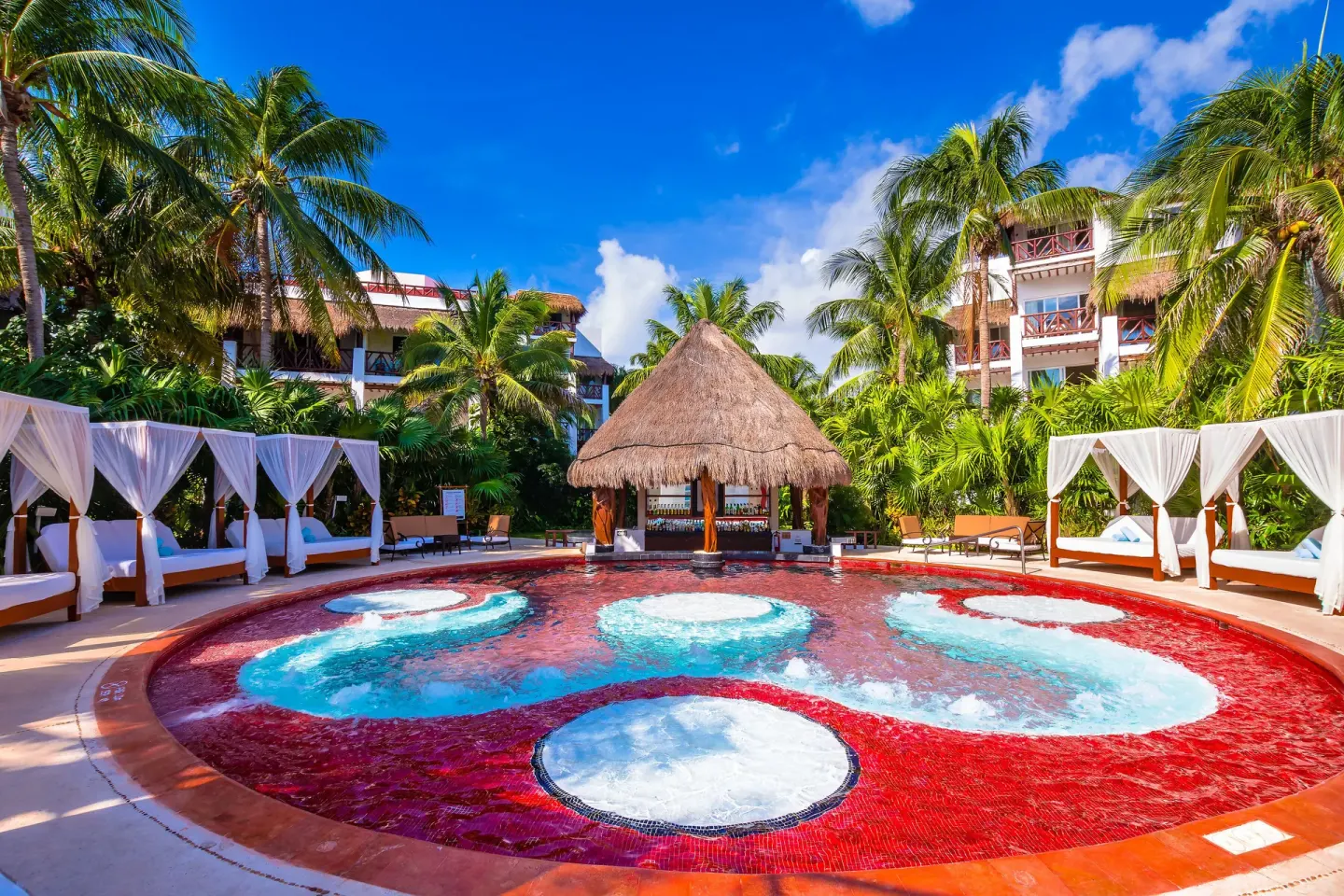 Circular red pool with white bubbling pads and cabanas at Desire Pearl Riviera Maya Resort.