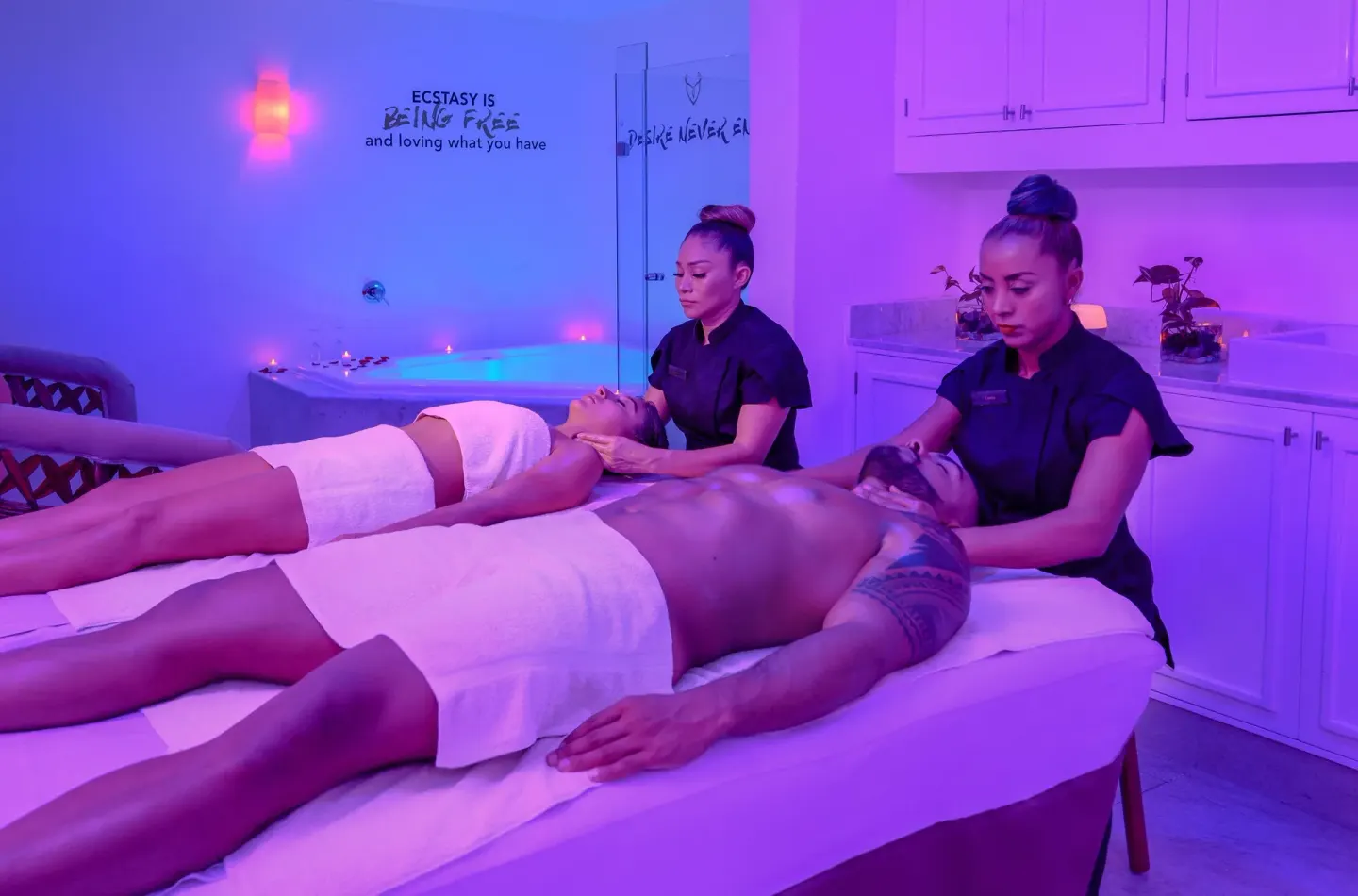 Couples massage tables in a purple-lit spa room at Desire Pearl Riviera Maya Resort.