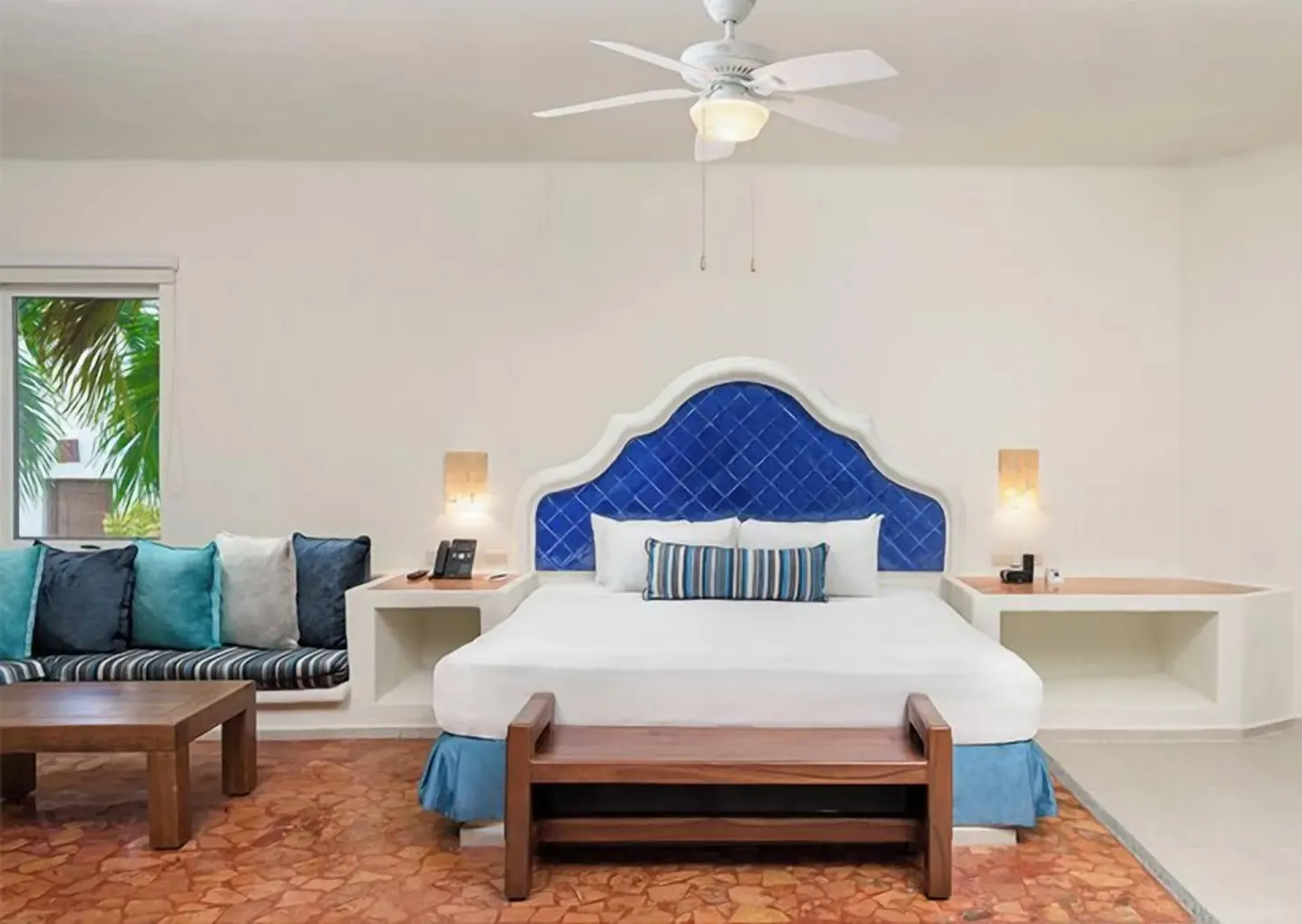 Guest room at Desire Pearl Riviera Maya Resort with king bed, blue headboard and built-in sofa.