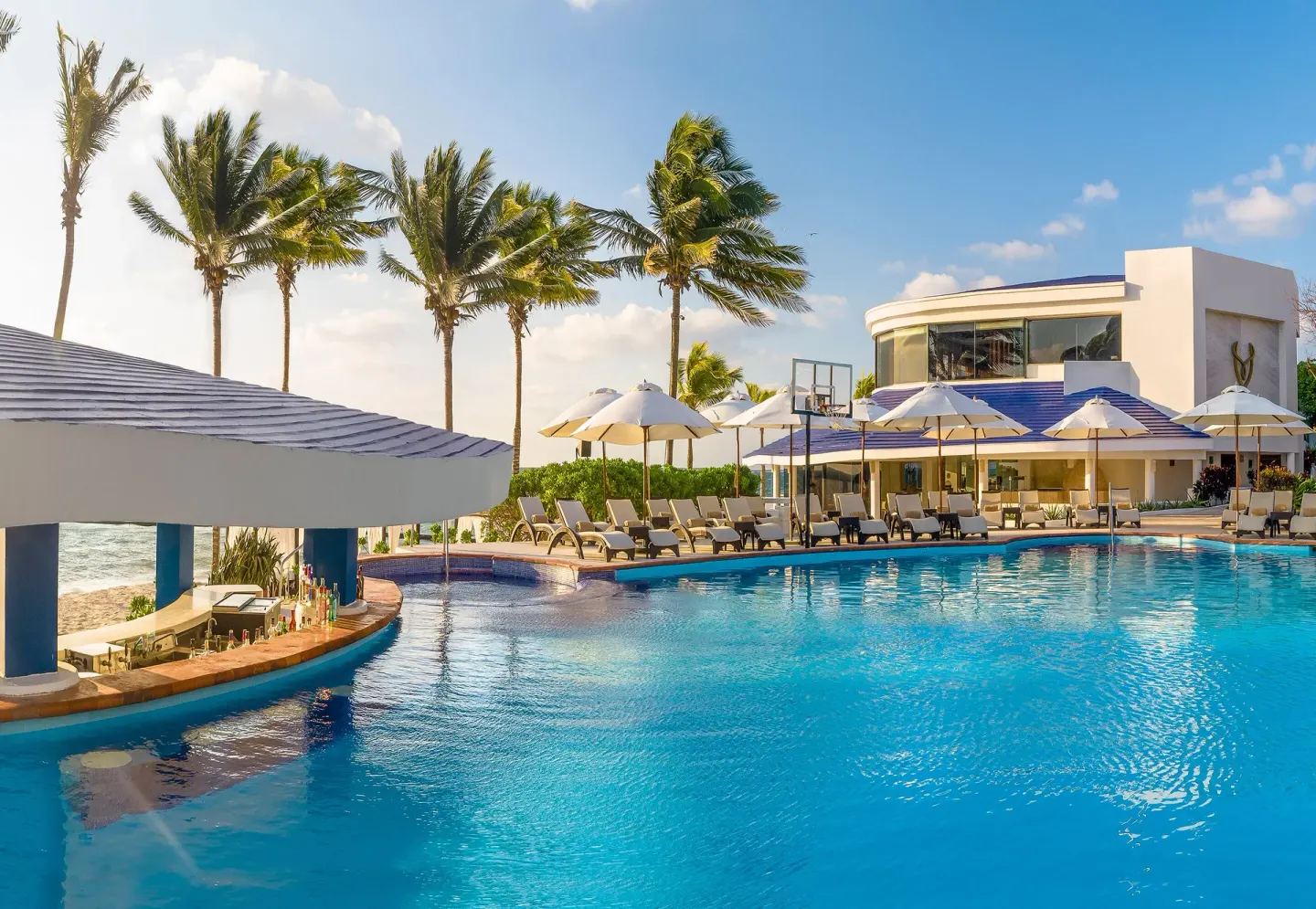 Pool with swim-up bar, loungers and palms at Desire Pearl Riviera Maya Resort.