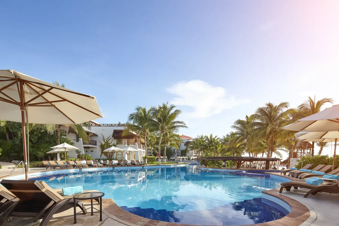 Large resort pool with loungers, umbrellas, and palms at Desire Pearl Riviera Maya Resort.