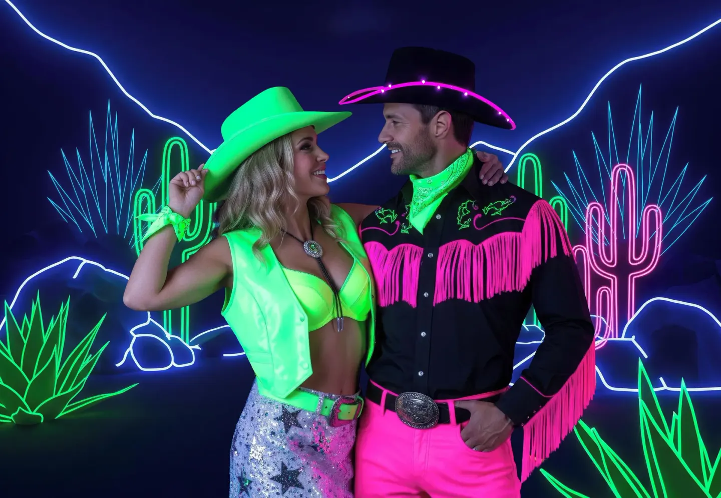 Couple in neon western costumes poses by cactus lights at Desire Pearl Riviera Maya Resort.