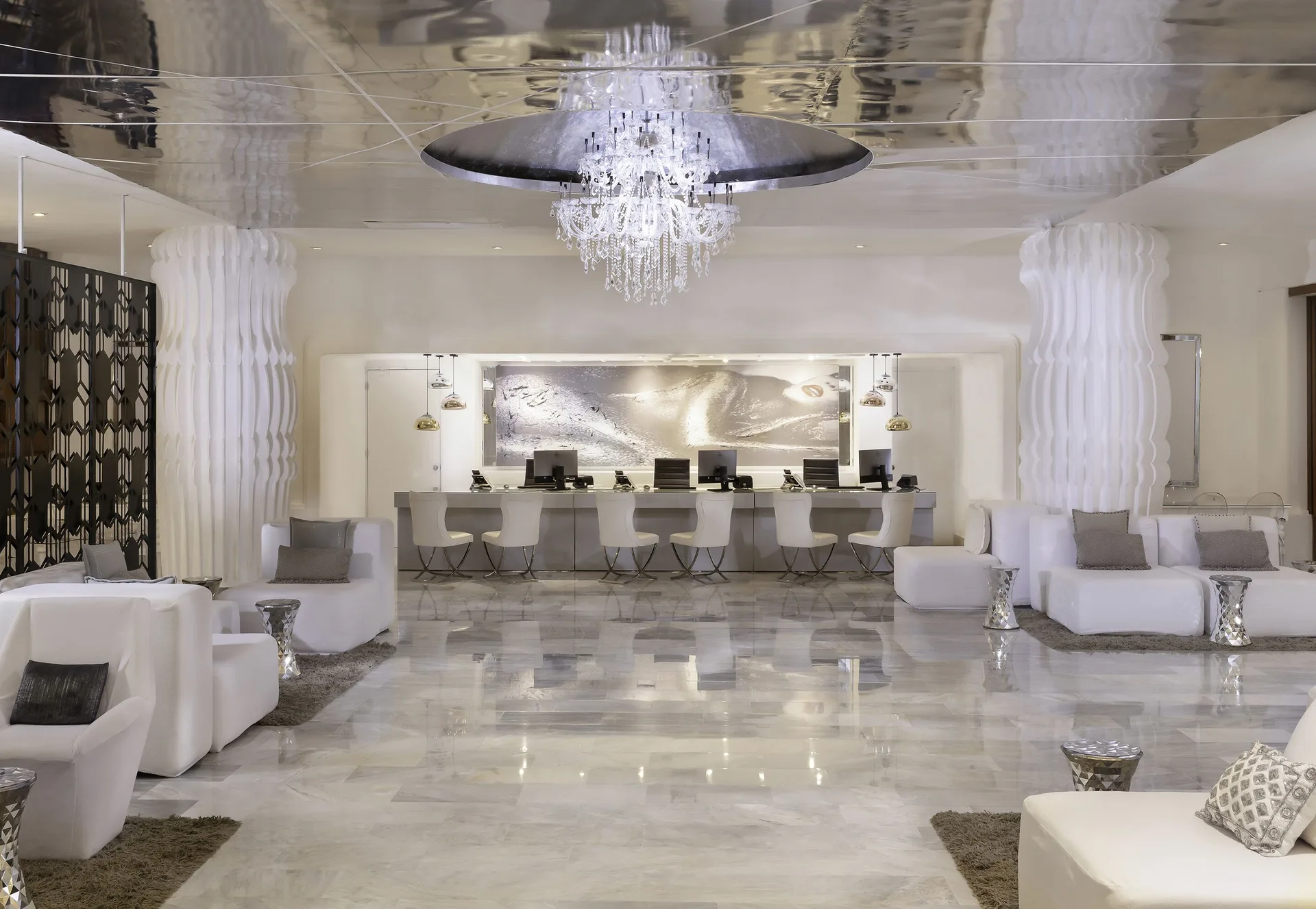 White lobby lounge at Desire Pearl Riviera Maya Resort with chandelier, sofas and reception desks.