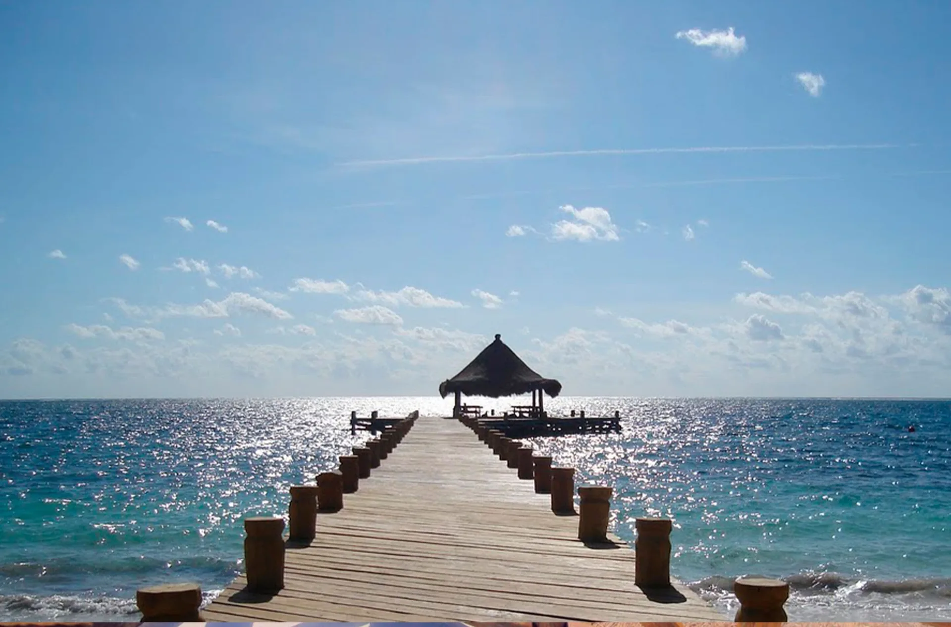 Wooden pier extends over turquoise sea at Desire Pearl Riviera Maya Resort.