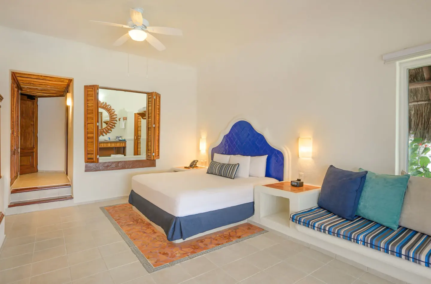 Junior Suite king bed, bench seating, and wood-framed mirror at Desire Pearl Riviera Maya Resort.