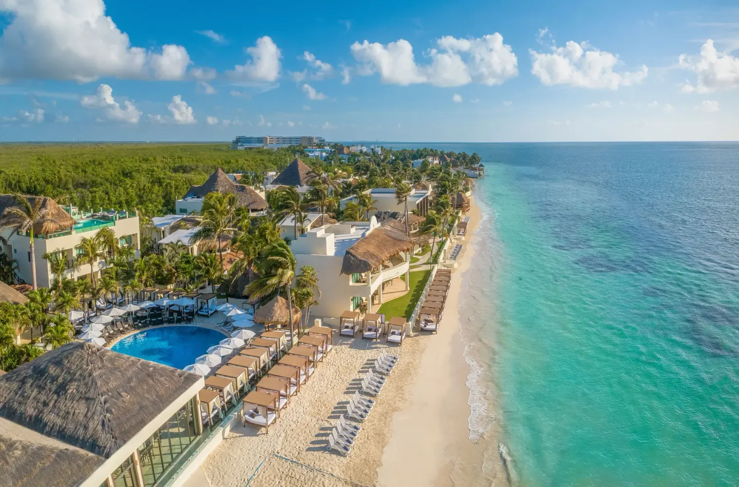 Aerial beachfront view of pools, palms, loungers and turquoise sea at Desire Riviera Maya Resort.