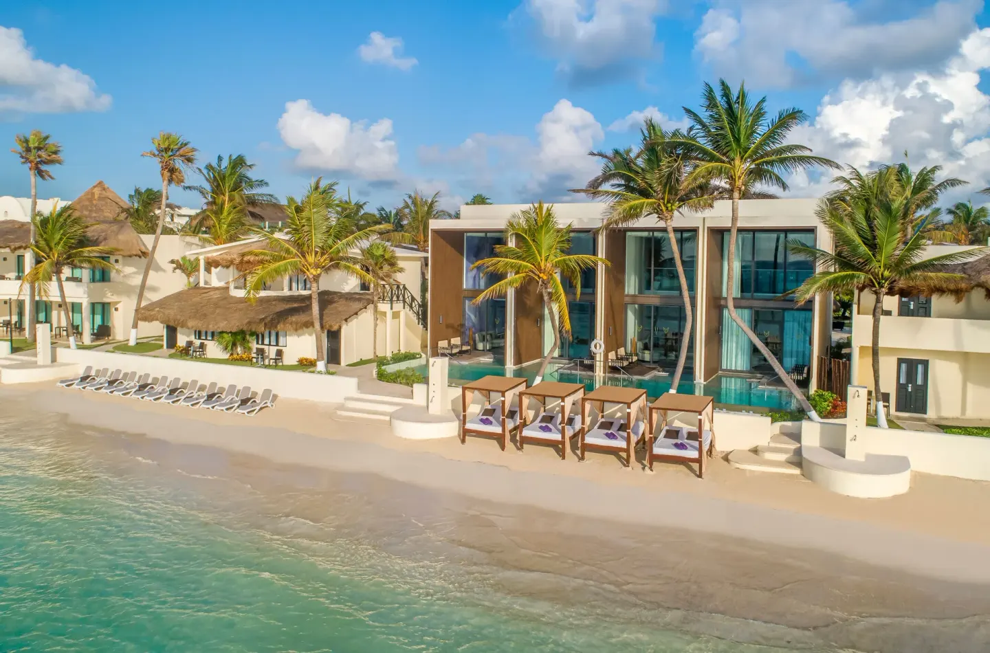 Palm-lined beachfront suites and cabanas along the shore at Desire Riviera Maya Resort.