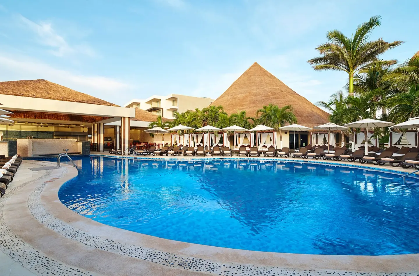 Curved outdoor pool with loungers, umbrellas, cabanas and palms at Desire Riviera Maya Resort.