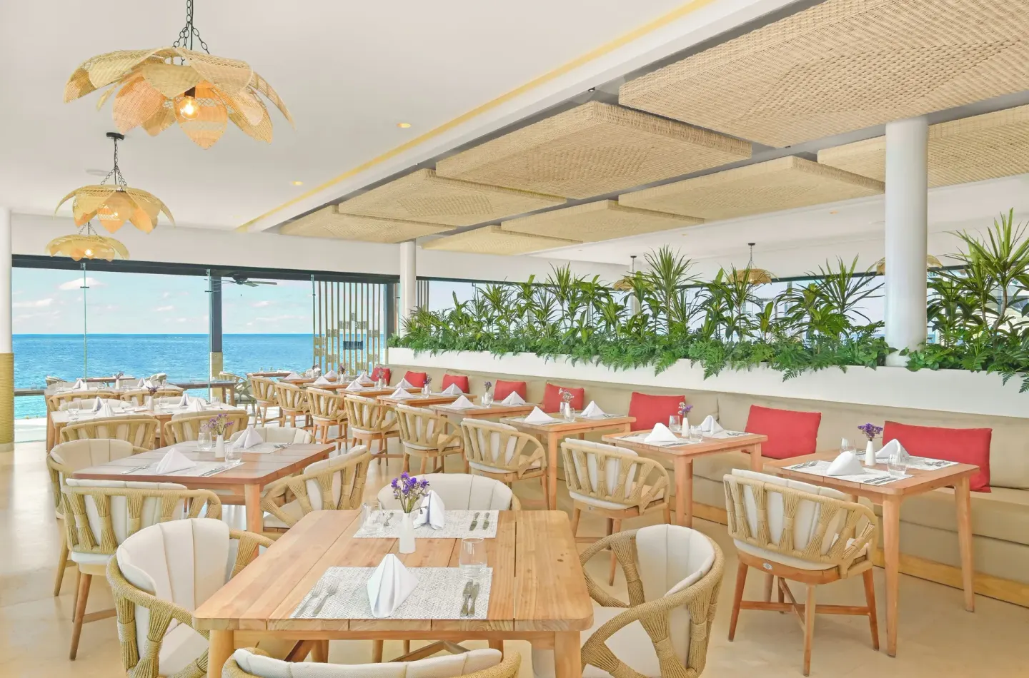 Oceanfront restaurant with light wood tables at Desire Riviera Maya Resort.