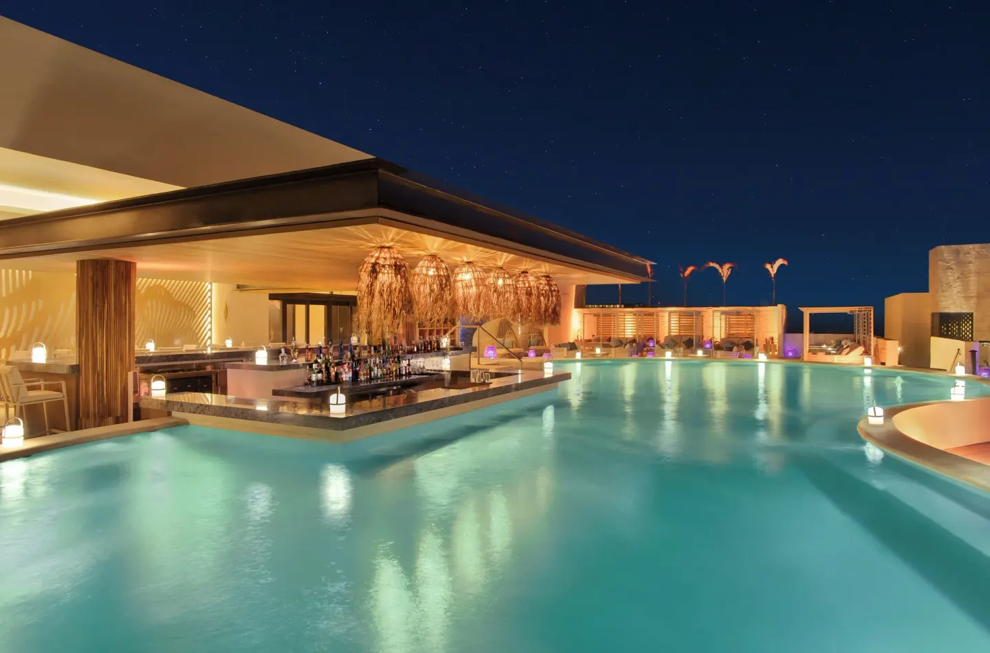 Rooftop pool bar glowing at night at Desire Riviera Maya Resort.